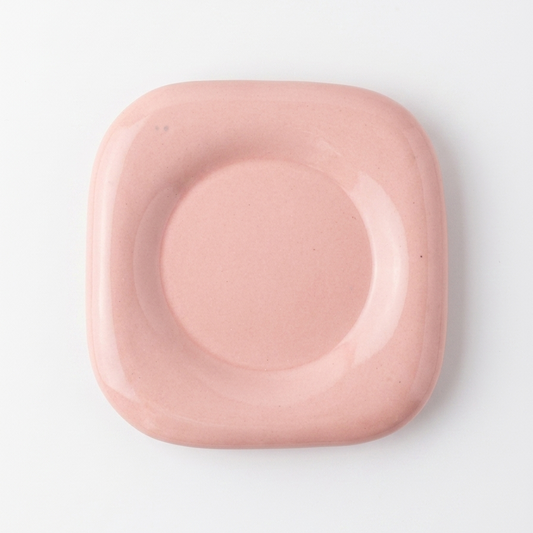 A square ceramic dish with rounded corners and a raised circular center, shown from a top-down view on a clean white background.