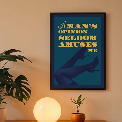 A framed art print with the text 'A MAN'S OPINION Seldom Amuses ME' in yellow over a dark teal background, hanging on a beige wall above a wooden console table with a glowing lamp and potted plants.