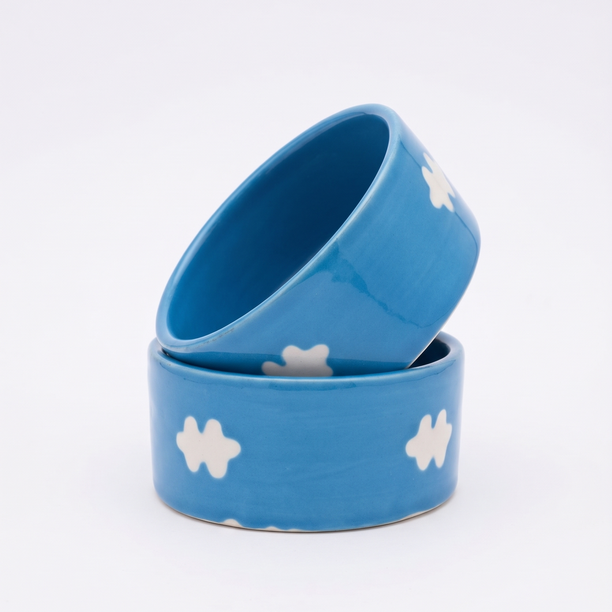 Two small ceramic bowls in a bright blue color with white cloud-like patterns, stacked on a clean white background.