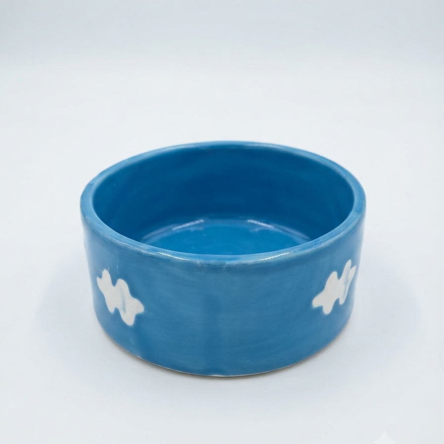 A blue ceramic bowl with white hand-painted cloud-like patterns on the sides, photographed on a seamless white background.