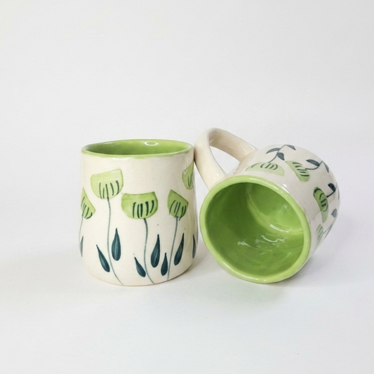Two ceramic mugs with green interior and floral design on a white background