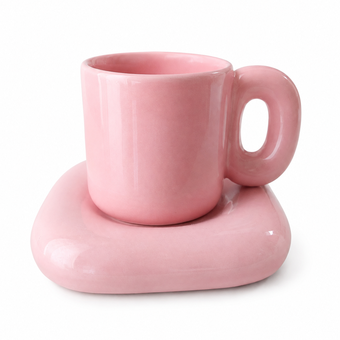 A glossy pink ceramic mug with a thick, rounded handle, resting on a matching thick, wavy pink ceramic base against a white background.