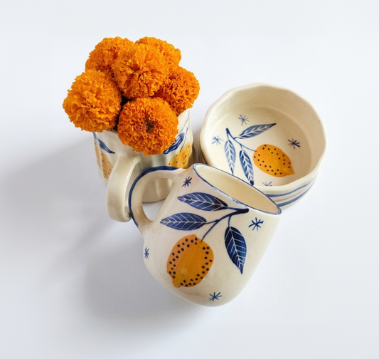 Ceramic mug, snack bowl and milk jar with orange and blue designs on a white background