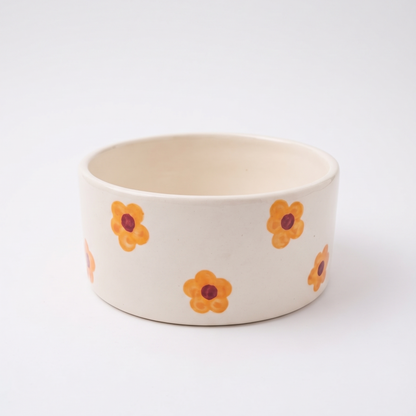An off-white ceramic bowl decorated with a pattern of small orange flowers with dark red centers, set against a clean white background.