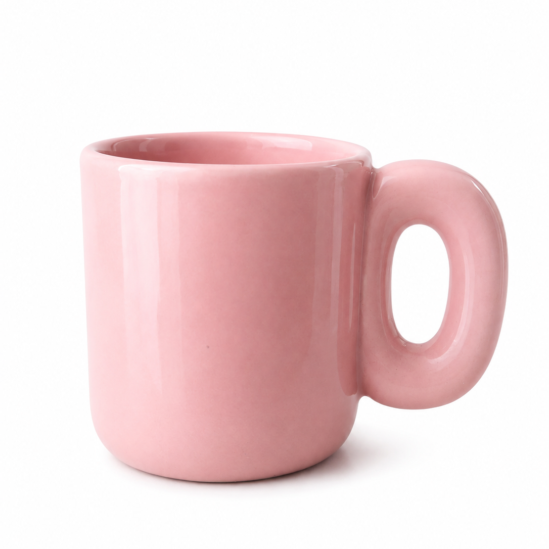 A glossy light pink ceramic mug with a unique rounded handle, shown on a clean white background.