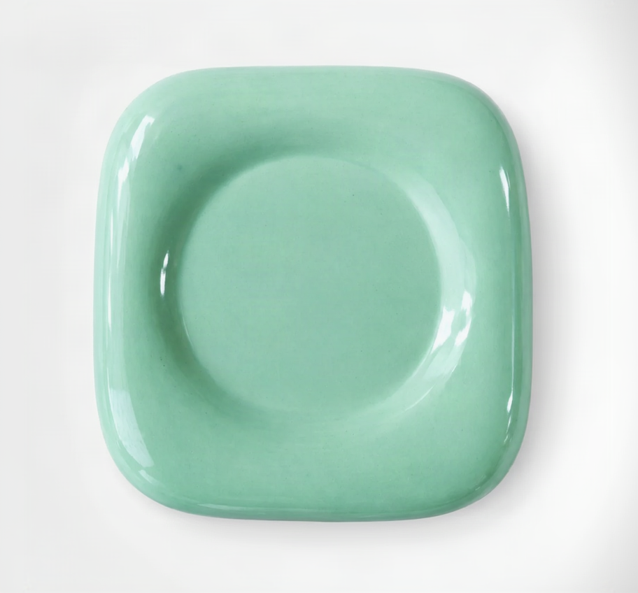 A glossy ceramic square plate with rounded corners and a raised circular center, shown from above on a white background.