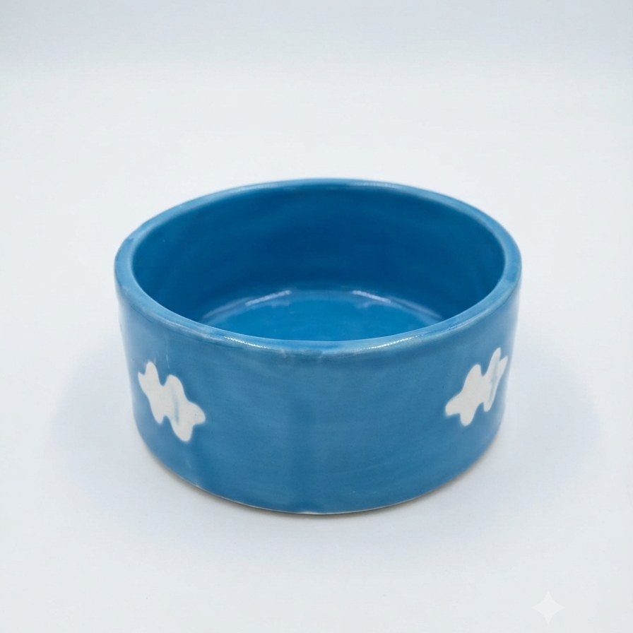 A blue ceramic bowl with white hand-painted cloud-like patterns on the sides, photographed on a seamless white background.