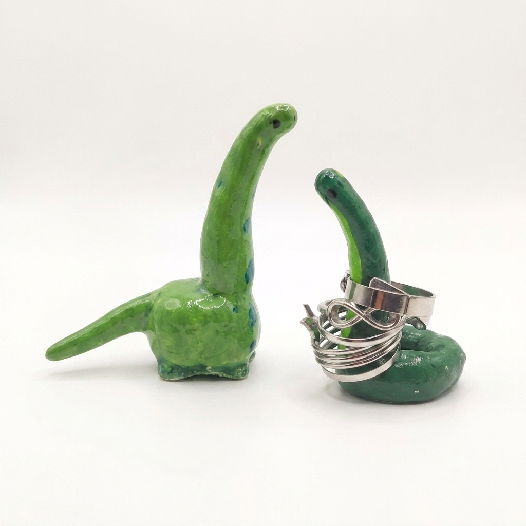 Two green ceramic objects shaped like dinosaurs with a silver ring holder on a white background