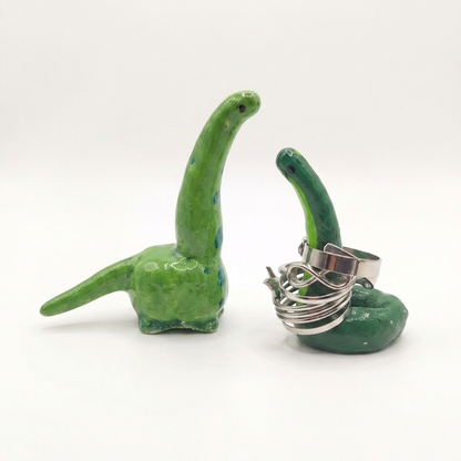Two green ceramic objects shaped like dinosaurs with a silver ring holder on a white background