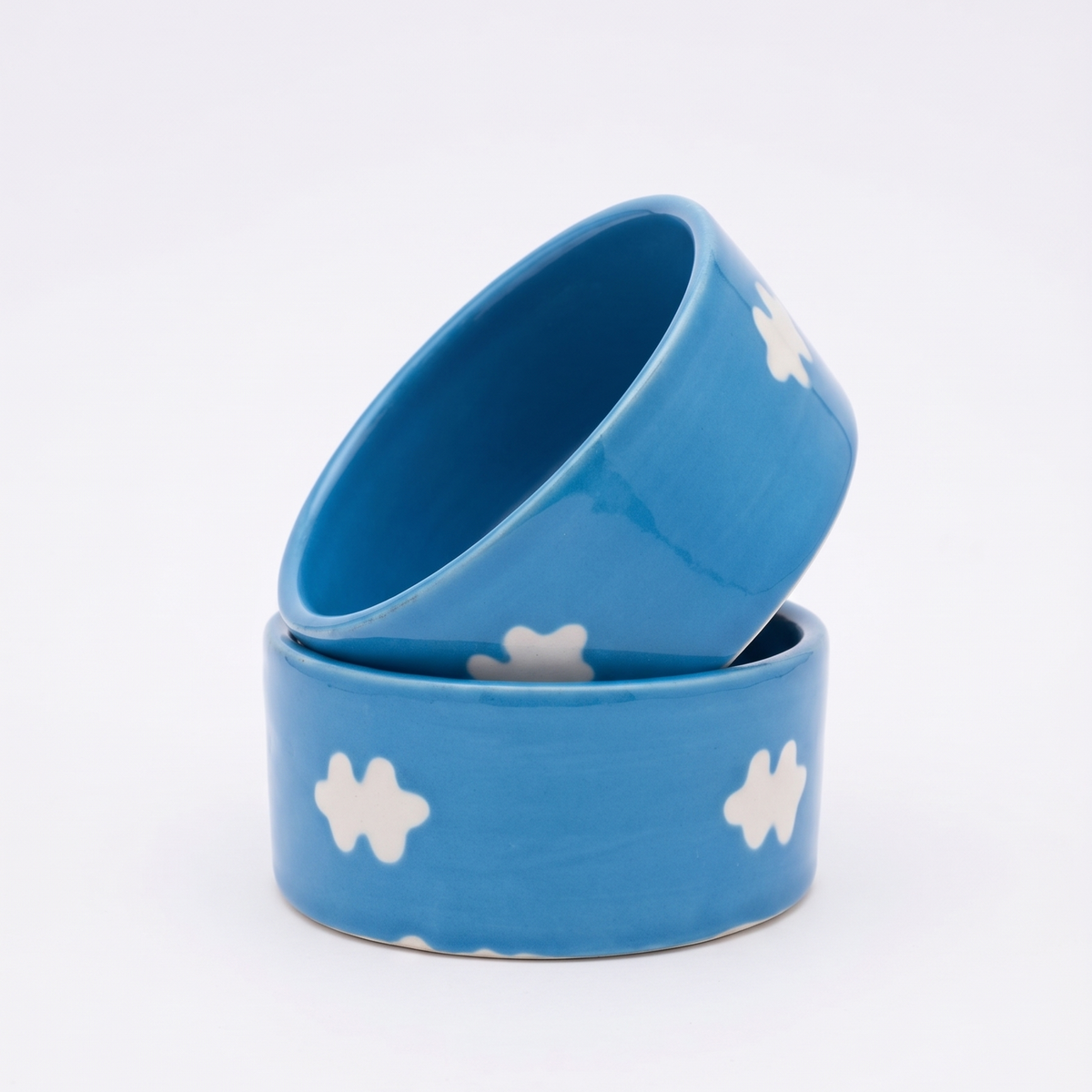 Two small ceramic bowls in a bright blue color with white cloud-like patterns, stacked on a clean white background.