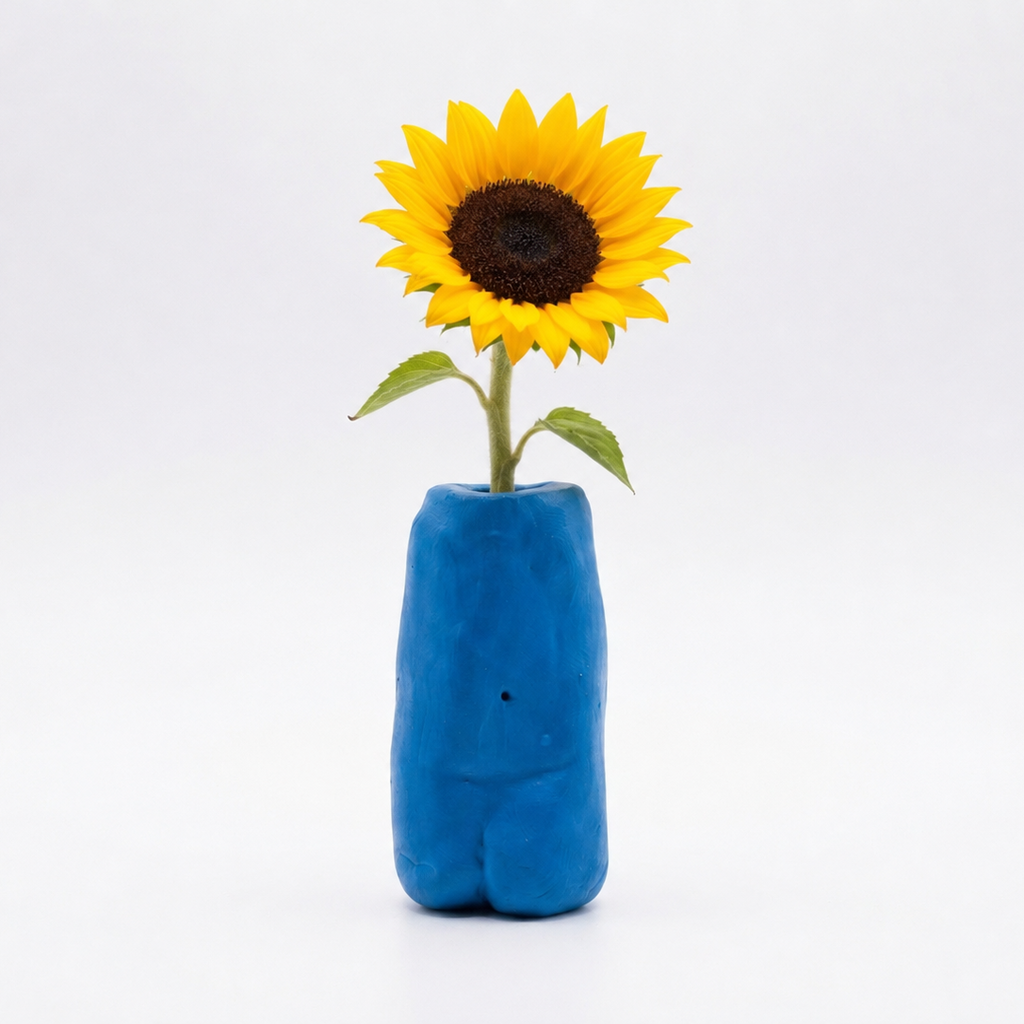 A single yellow sunflower with a dark brown center and green stem, placed in a small sculptural blue vase against a clean white background.