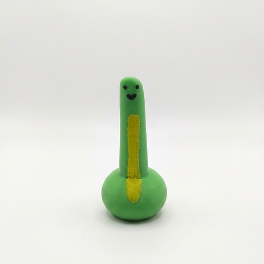 A small green dinosaur-shaped toy with a yellow belly stripe, black facial features, and a round base, photographed against a plain light gray background.