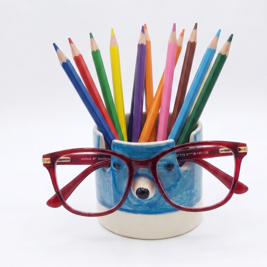 A ceramic pencil holder shaped like a blue polar bear face, filled with colorful colored pencils and topped with red eyeglasses, photographed on a clean white background.