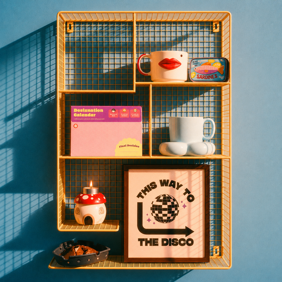 A yellow wire shelving unit mounted on a blue wall, styled with various decorative items including mugs, a calendar, a small mushroom-shaped candle, and a framed disco-themed print.